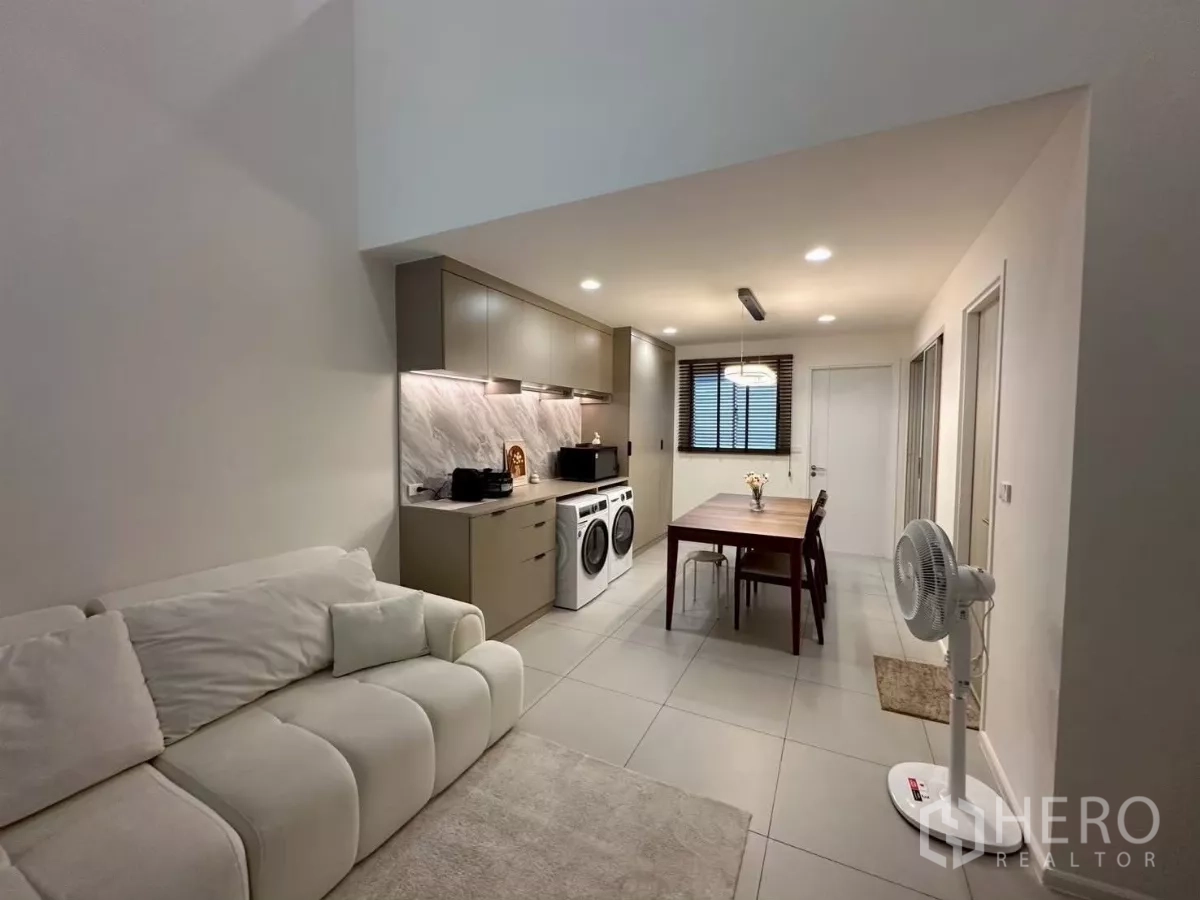 Townhouse for rent in Saphan Sung, Bangkok - Open-plan living, dining and pantry area with a plush sofa, wood dining table and recessed lighting.