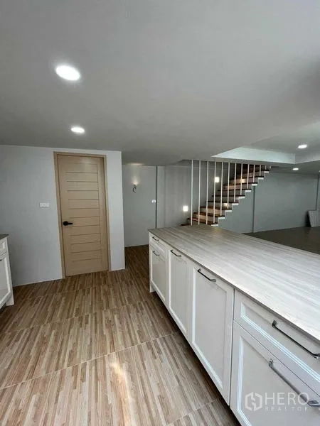 Townhouse for sale in Phra Khanong, Bangkok - Open-plan kitchen with white cabinets, wood countertop and a staircase in a renovated Phra Khanong townhouse.