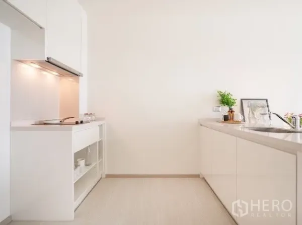 Condominium for sale in Khlong Toei, Bangkok - Modern white kitchen with under-cabinet lighting, sink, and open shelving for storage.