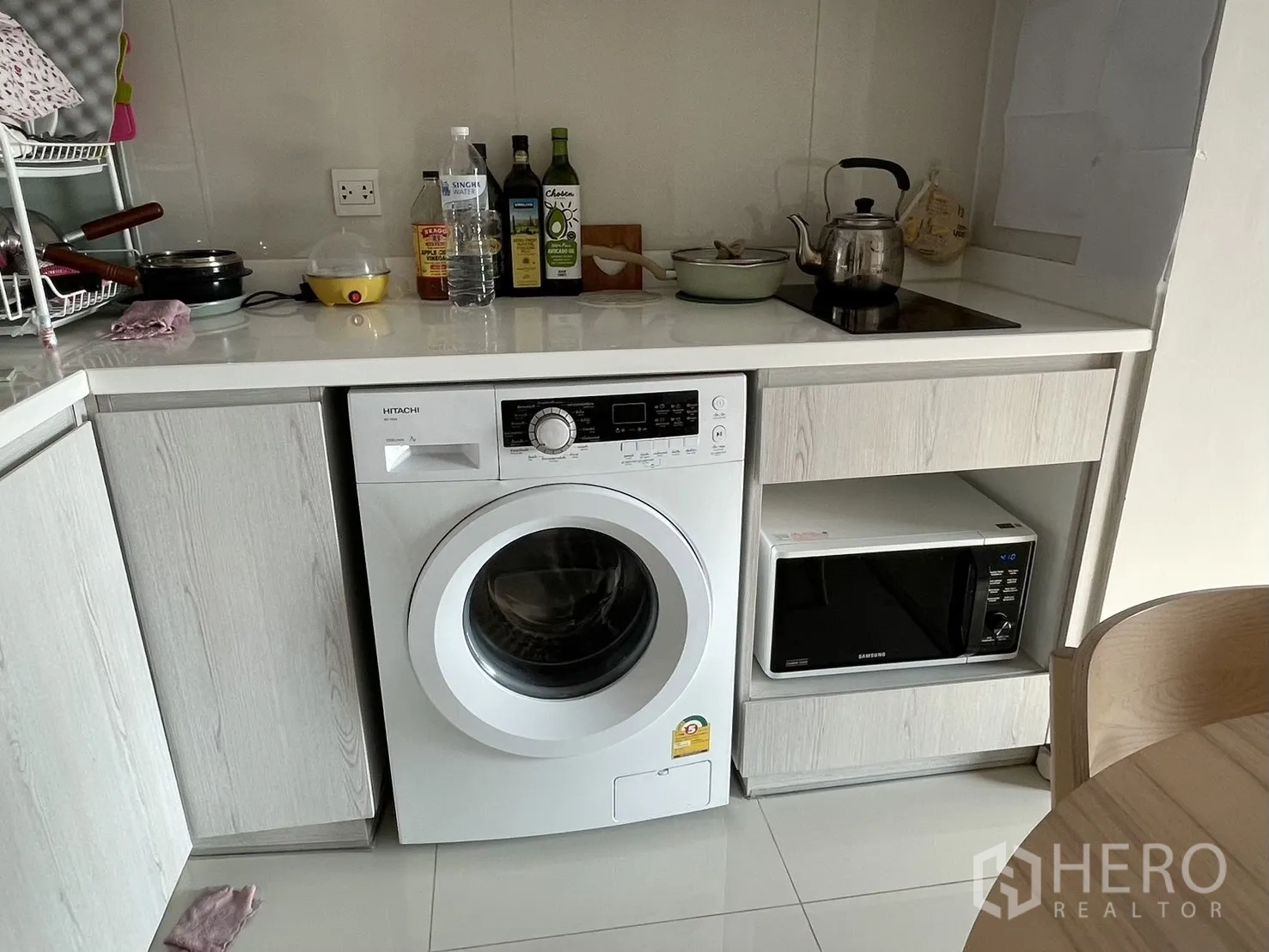 公寓 for rent in Pathum Wan, Bangkok - 紧凑L形厨房，内置洗衣机、微波炉与电磁炉，配白色橱柜台面。
