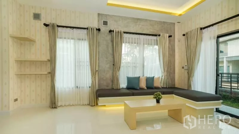 独立式住宅 出售在Lat Krabang, Bangkok - 现代客厅，L形内置沙发与茶几，落地窗通向花园。