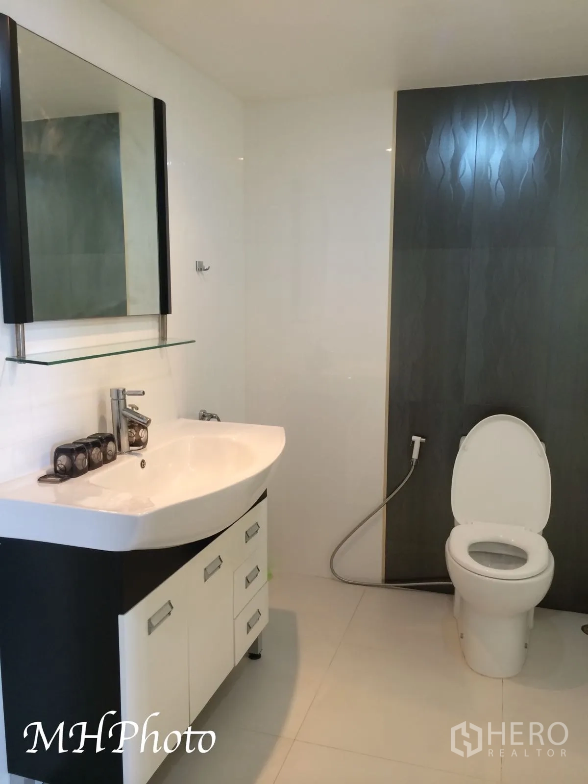 Condominium for rent in Watthana, Bangkok - Contemporary bathroom with vanity, mirror, toilet and handheld bidet in white and gray tones.