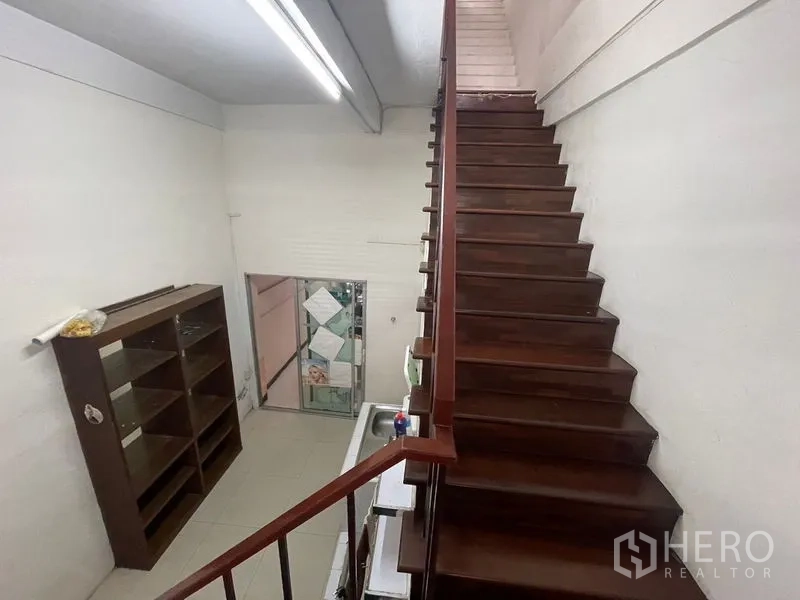 Shophouse for rent in Phra Khanong, Bangkok - Wooden staircase ascending beside a sink and open shelving.