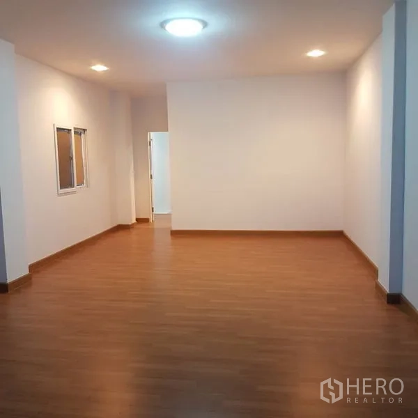 Home Office for sale in Lat Phrao, Bangkok - Open-plan room with recessed lighting, wood floors, and a doorway to a utility area.