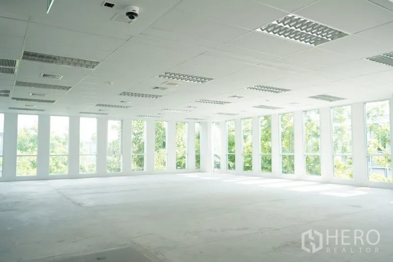 办公空间 出租在Bang Na, Bangkok - 采光充足的开放式办公室，落地窗与白色格栅天花、照明设备，窗外绿景，临近BTS Bearing。