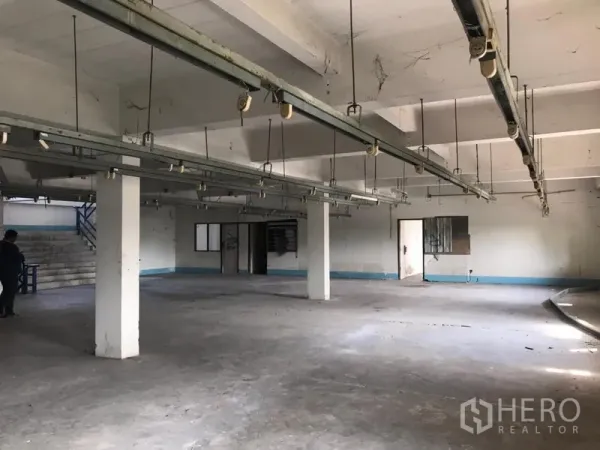 Warehouse for rent in Bueng Kum, Bangkok - Large production floor with hanging rails, concrete slab, columns, side office rooms and stair access within the warehouse.