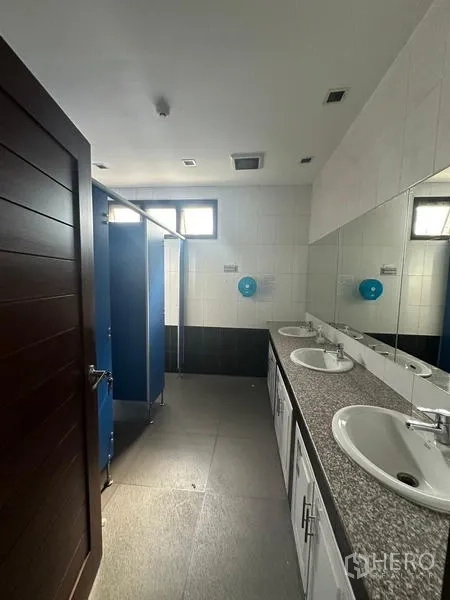 Warehouse for rent in Prawet, Bangkok - Restroom with double sinks, large mirror, and blue-door stalls.
