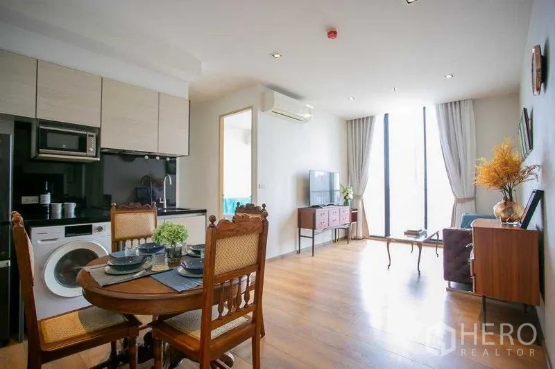 Condominium for sale in Khlong Toei, Bangkok - Open-plan living and dining area with floor-to-ceiling windows, wood floors, and a compact kitchen.