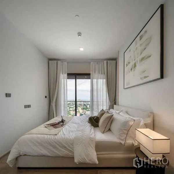 公寓 出租在Chatuchak, Bangkok - 极简卧室，大窗与柔和床品，俯瞰乍都节城市景色。
