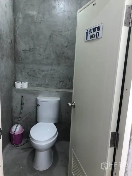 Warehouse for rent in Bang Yai, Nonthaburi - Clean men’s restroom with modern toilet, spray hose and polished concrete walls.