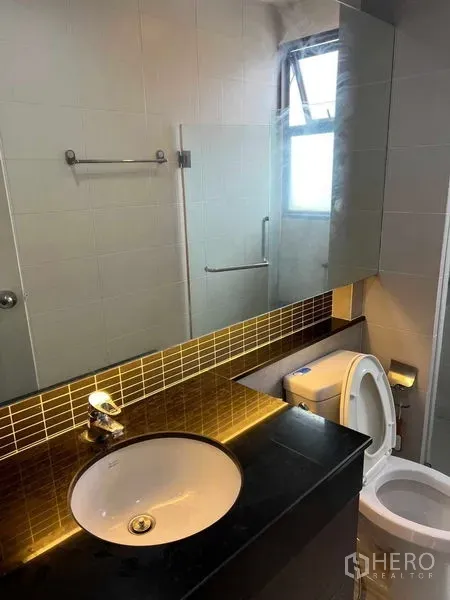 Townhouse for rent in Phra Khanong, Bangkok - Bathroom with black stone countertop, backlit mirror, toilet and a windowed shower area.