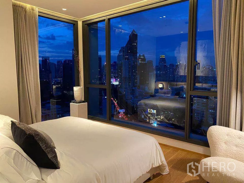 Condominium for rent or sale in Khlong Toei, Bangkok - Bedroom at night with panoramic floor‑to‑ceiling windows overlooking the illuminated skyline.