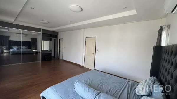 Detached House for sale in Lat Krabang, Bangkok - Spacious master bedroom with wood flooring, tufted headboard and mirrored wardrobes.