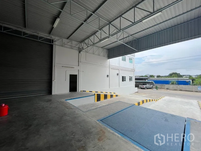 Warehouse for rent in Lat Krabang, Bangkok - Covered truck loading bay with dock leveler ramps, safety markings, and a roller shutter door at the warehouse entrance.
