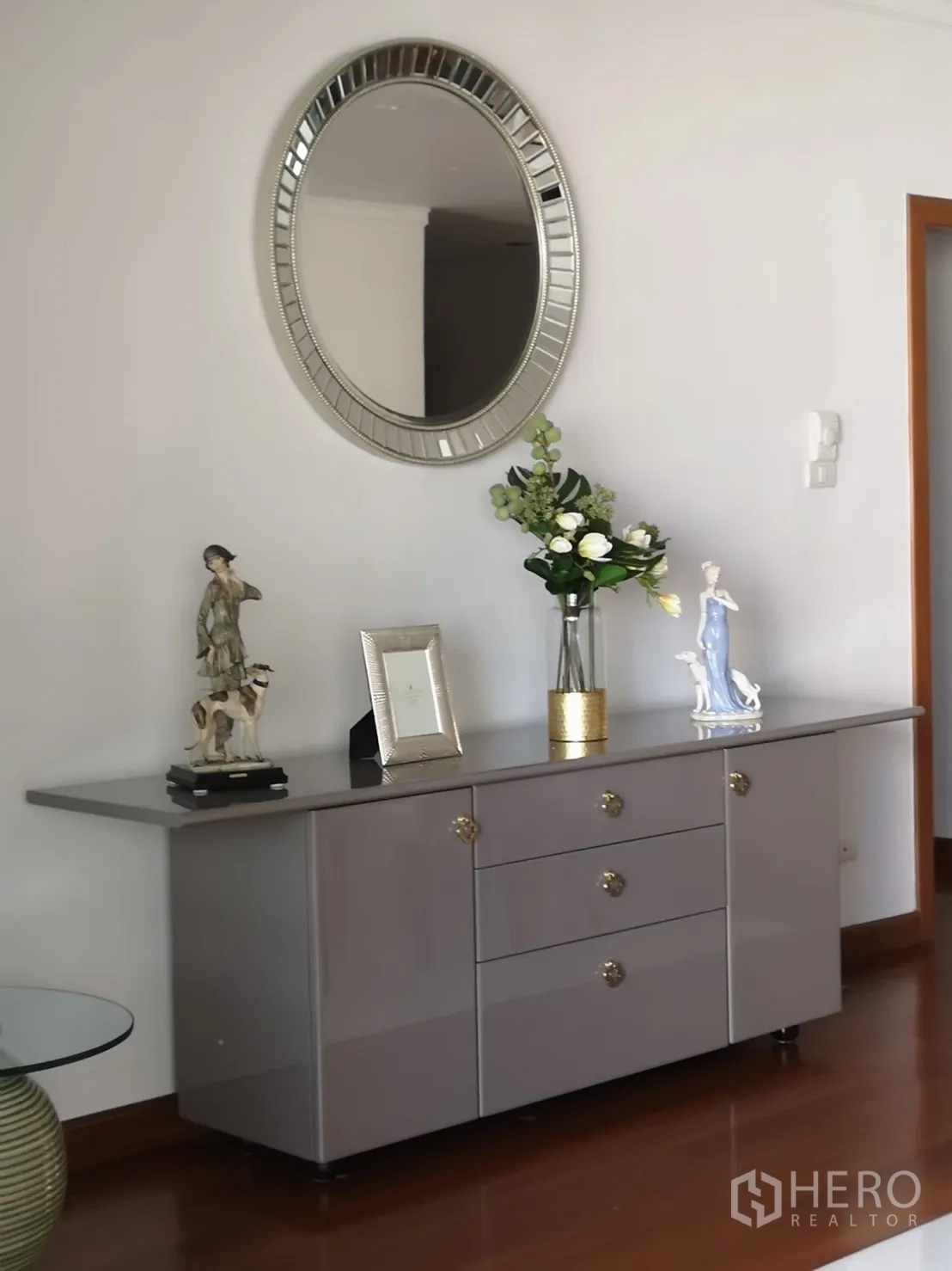 Condominium for rent in Bangkok - Elegant sideboard with round mirror and decorative accents on a white wall.