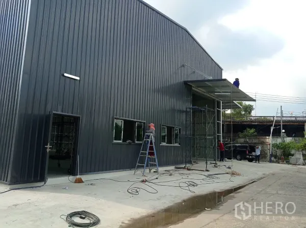 คลังสินค้า ให้เช่าในBang Kapi, Bangkok - ด้านข้างอาคารผนังเมทัลชีทสีเข้ม มีหน้าต่างและทางเดินคอนกรีต