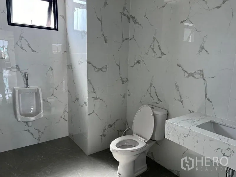 Warehouse for rent in Bang Sao Thong, Samut Prakan - Clean tiled restroom with toilet, urinal and integrated basin inside the warehouse.