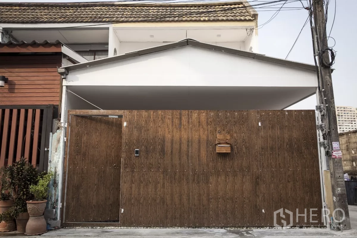 Townhouse for rent in Din Daeng, Bangkok - Front exterior of the two-storey townhouse featuring a tall wooden privacy gate and covered carport.