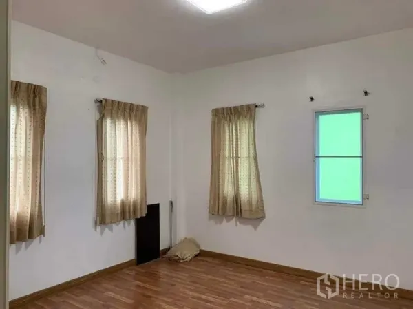 Detached House for sale in Sai Mai, Bangkok - Bright empty bedroom with white walls, wood flooring and curtained windows.