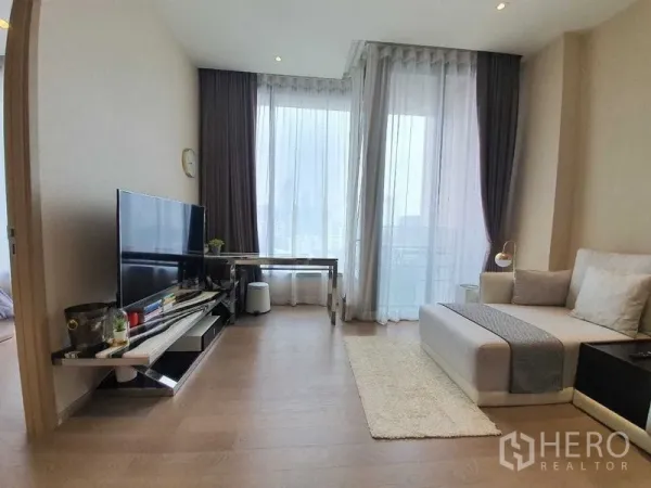 公寓 出租或出售在Watthana, Bangkok - 明亮客厅，落地窗、电视柜与工作桌，连通阳台可观城市景观。