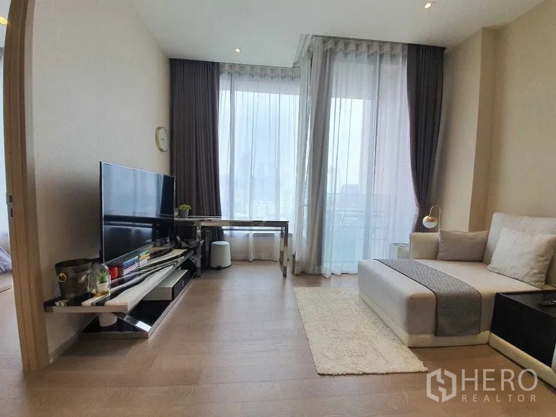 公寓 出租或出售在Watthana, Bangkok - 明亮客厅，落地窗、电视柜与工作桌，连通阳台可观城市景观。