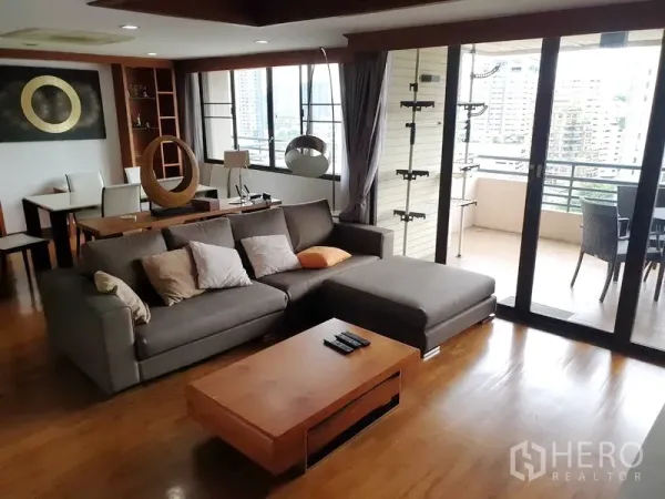 公寓 出租在Watthana, Bangkok - 开放式客厅，灰色转角沙发与木地板，落地推拉门通往观景阳台。