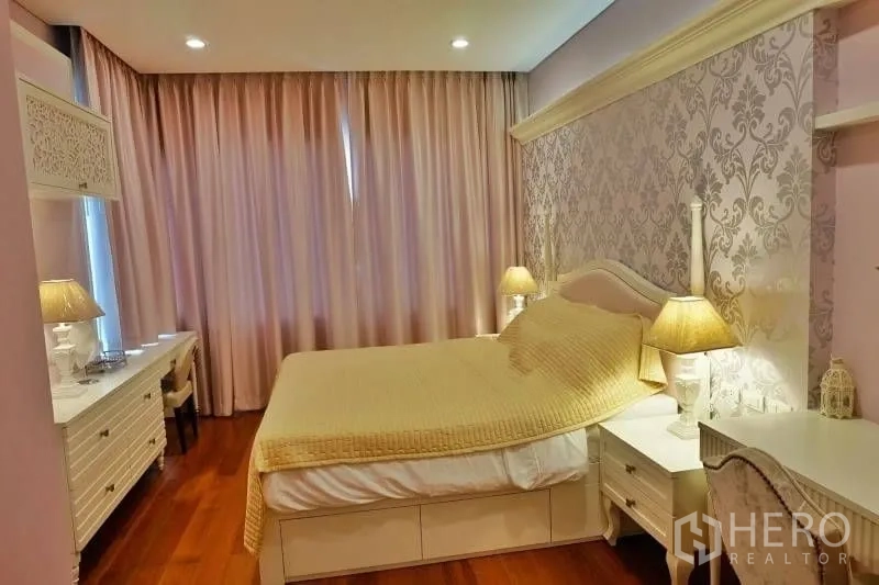 Condominium for rent in Khlong Toei, Bangkok - Guest bedroom in soft pastel tones with patterned wallpaper, bedside lamps, desk and chair.