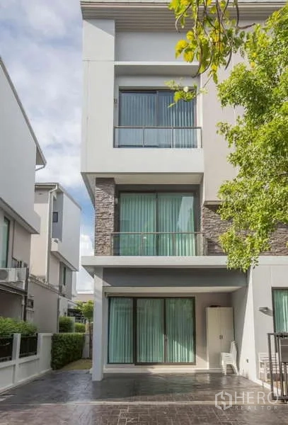 Detached House for rent or sale in Lat Phrao, Bangkok - Three-storey modern detached house facade with large windows and a balcony in Lat Phrao, Bangkok.