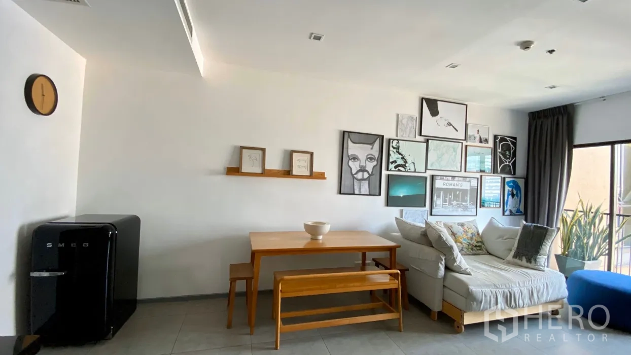Condominium for rent in Bangkok - Bright living and dining area with gallery wall, wooden table and bench, sofa, and a balcony with plants in a modern Bangkok condo.