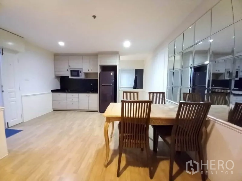 Condominium for rent in Khlong Toei, Bangkok - Dining area with a wooden table for four beside a mirrored wall and open kitchen.