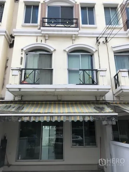 Townhouse for rent or sale in Bang Kapi, Bangkok - Three-storey townhouse facade with balconies and striped awning in Bang Kapi, Bangkok.