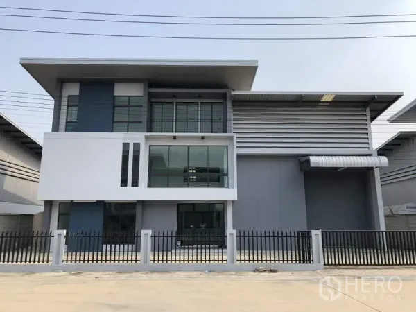 Warehouse for rent or sale in Lam Luk Ka, Pathum Thani - Modern warehouse with three-storey office facade, large windows and secure front fence in a Lam Luk Ka industrial compound.