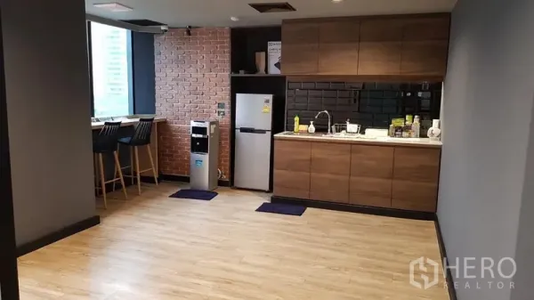 Office Space for rent in Khlong Toei, Bangkok - Modern office pantry with wooden cabinets, black subway-tile backsplash, brick accent wall, bar seating and refrigerator.