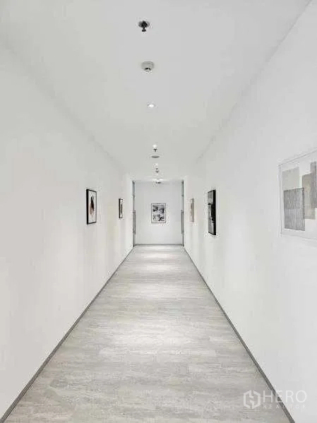 Office Space for rent in Bang Rak, Bangkok - Clean white corridor with recessed lighting and framed artwork leading to offices.