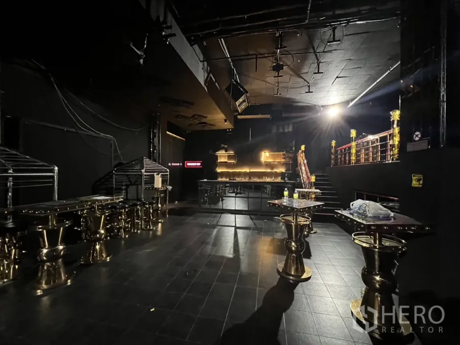 Retail Space for rent - Main floor showing an illuminated back bar, gold cocktail tables, and stairs to the mezzanine.