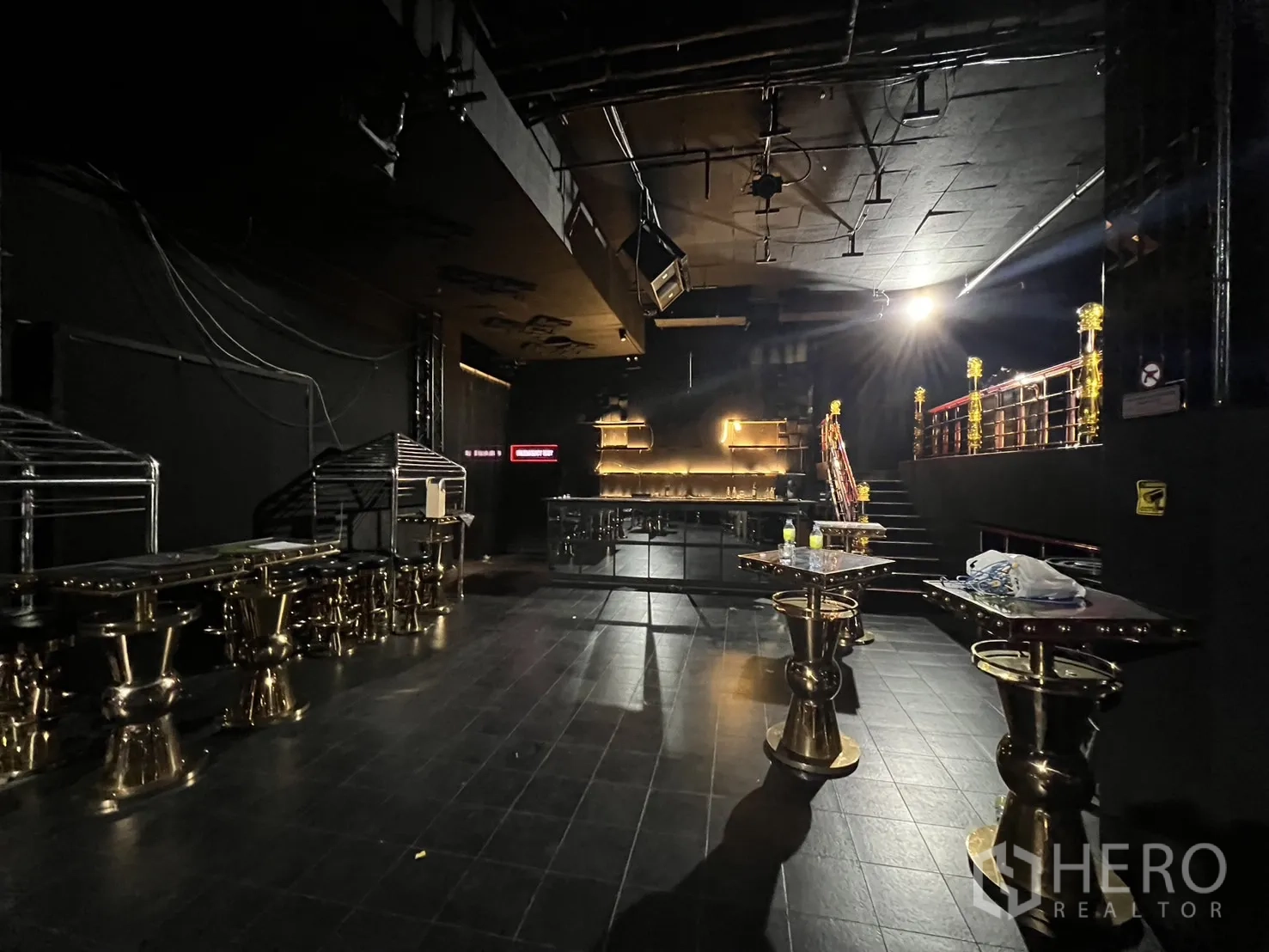 Retail Space for rent - Main floor showing an illuminated back bar, gold cocktail tables, and stairs to the mezzanine.