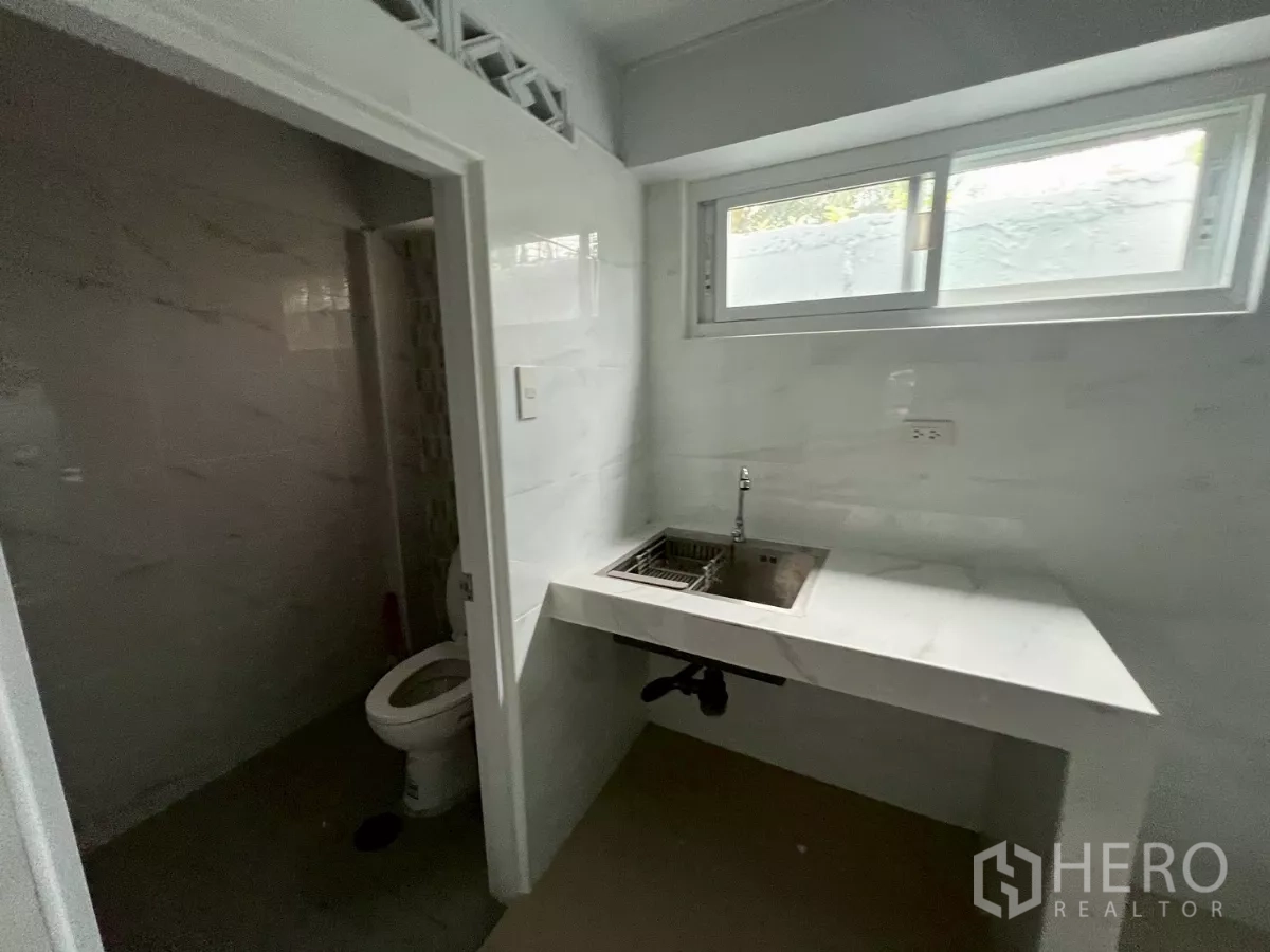 Shophouse for rent in Khlong Toei, Bangkok - Close-up of white countertop sink beneath a sliding window beside a bathroom door.