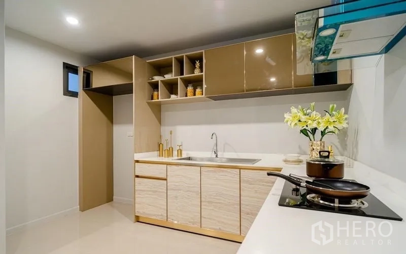 Detached House for sale in Lam Luk Ka, Pathum Thani - Compact L-shaped kitchen with cooktop, range hood, and ample storage cabinets.