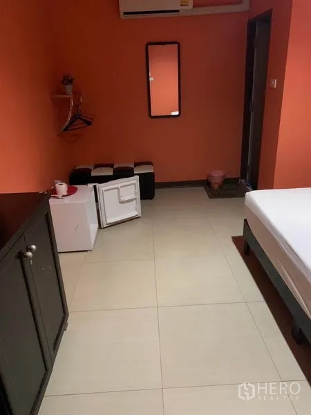 Retail Space for rent in Khlong Toei, Bangkok - Guest room with orange walls, mini fridge, mirror and small stools.