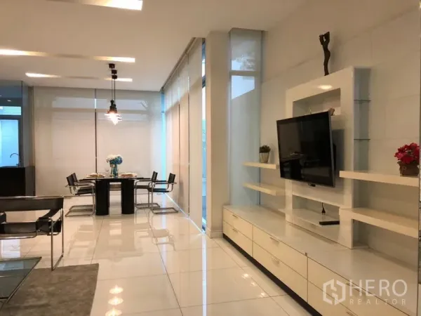 Townhouse for rent or sale in Chatuchak, Bangkok - Built-in TV wall with shelving beside a dining set in a minimalist living space.