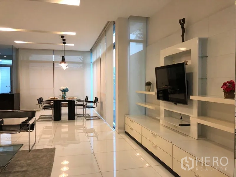Townhouse for rent or sale in Chatuchak, Bangkok - Built-in TV wall with shelving beside a dining set in a minimalist living space.