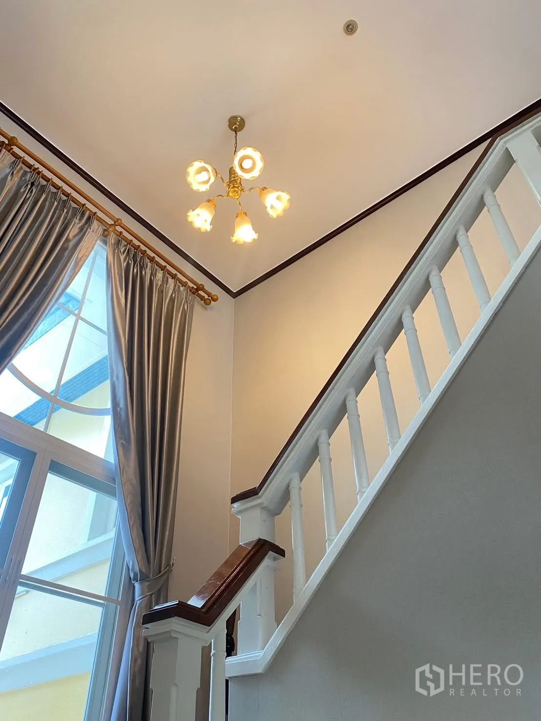 Detached House for rent in Phra Khanong, Bangkok - Staircase with white balustrade beside an arched window with curtains and a ceiling light.