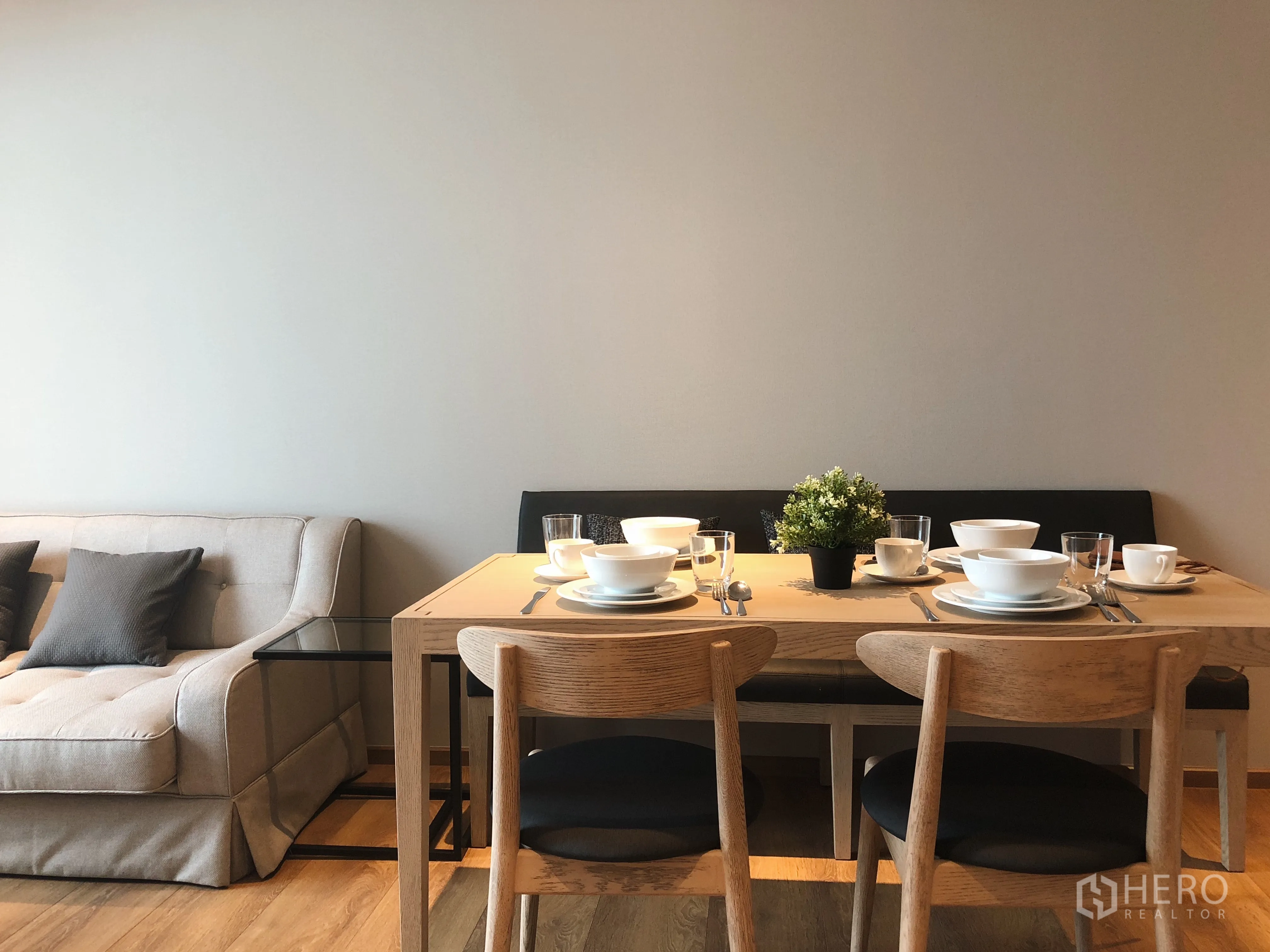 Condominium for rent in Khlong Toei, Bangkok - Wood dining table set for four beside sofa in the open-plan living area.