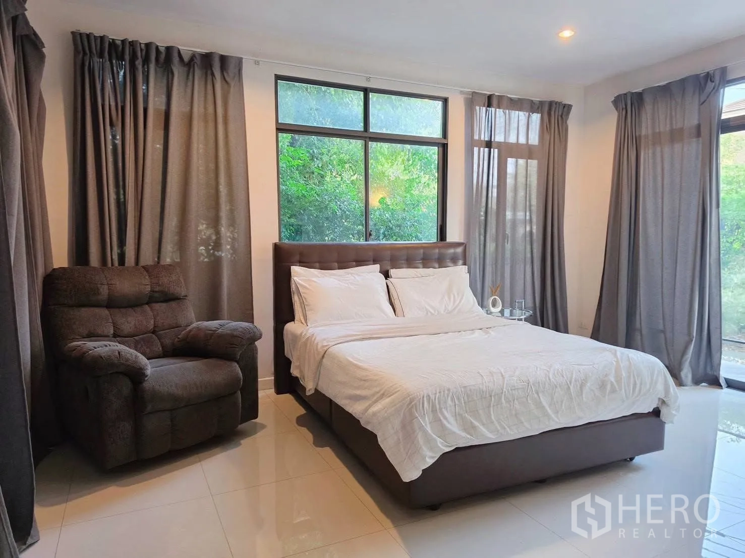 บ้านเดี่ยว for rent or sale in Suan Luang, Bangkok - ห้องนอนมุมบ้านหน้าต่างบานใหญ่ เตียงและเก้าอี้เอน