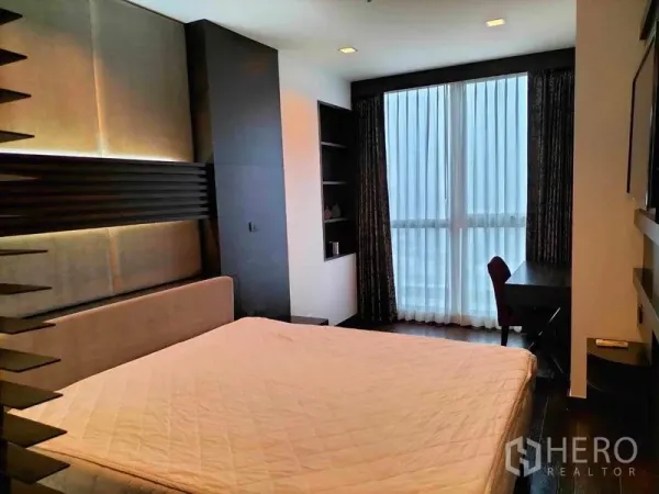 Condominium for rent in Ratchathewi, Bangkok - Bedroom with desk by floor-to-ceiling window, built-in shelves and city-facing balcony doors.