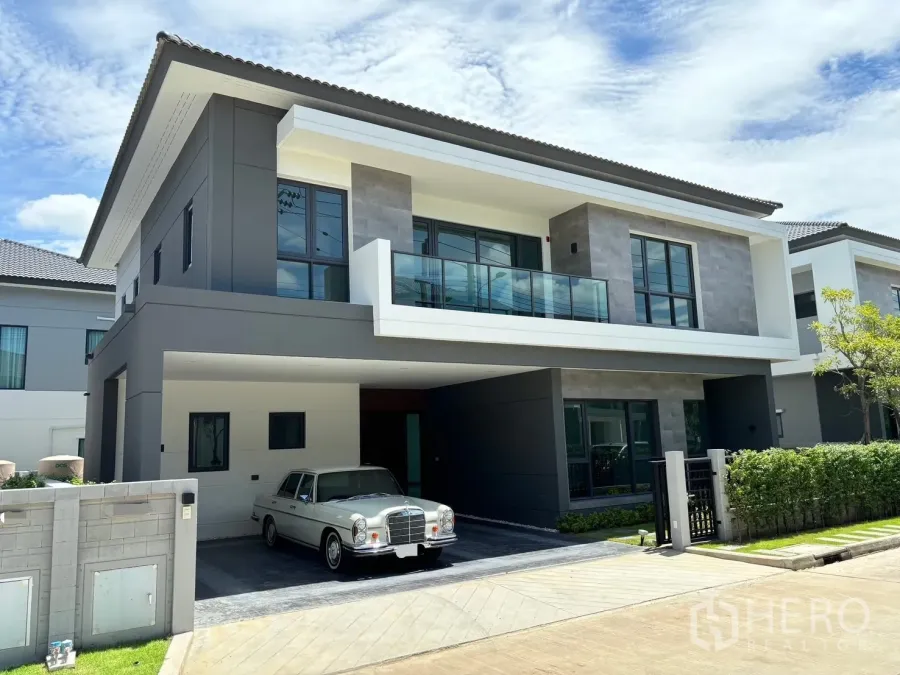 Townhouse for rent - Modern two‑storey townhouse exterior with covered carport, glass balcony and landscaped hedge under a blue sky.
