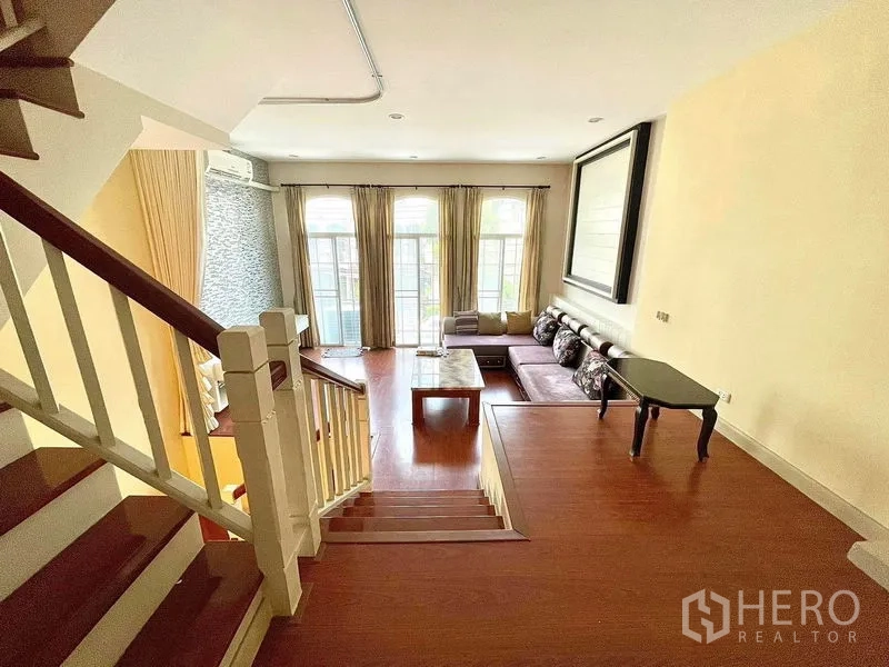Townhouse for rent in Saphan Sung, Bangkok - Elevated living area with large French windows, curtains, L‑shaped sofa and wood flooring.