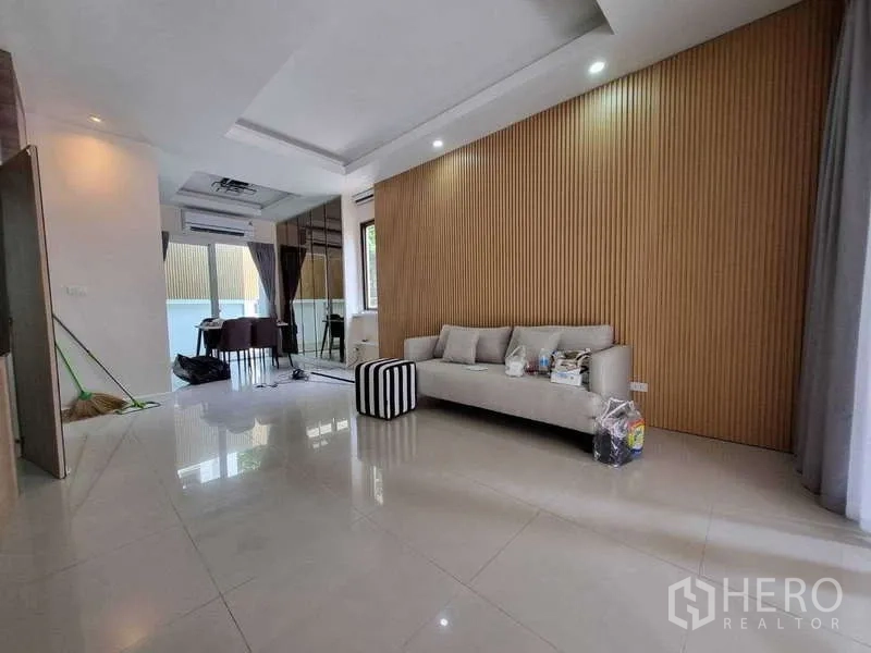 联排别墅 出租在Wang Thonglang, Bangkok - 开放式客餐厅，沙发、木纹格栅墙与亮面地砖。