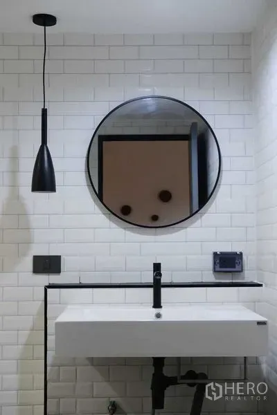 Condominium for rent in Bang Rak, Bangkok - Bathroom vanity with round mirror and black pendant light against tiled walls.