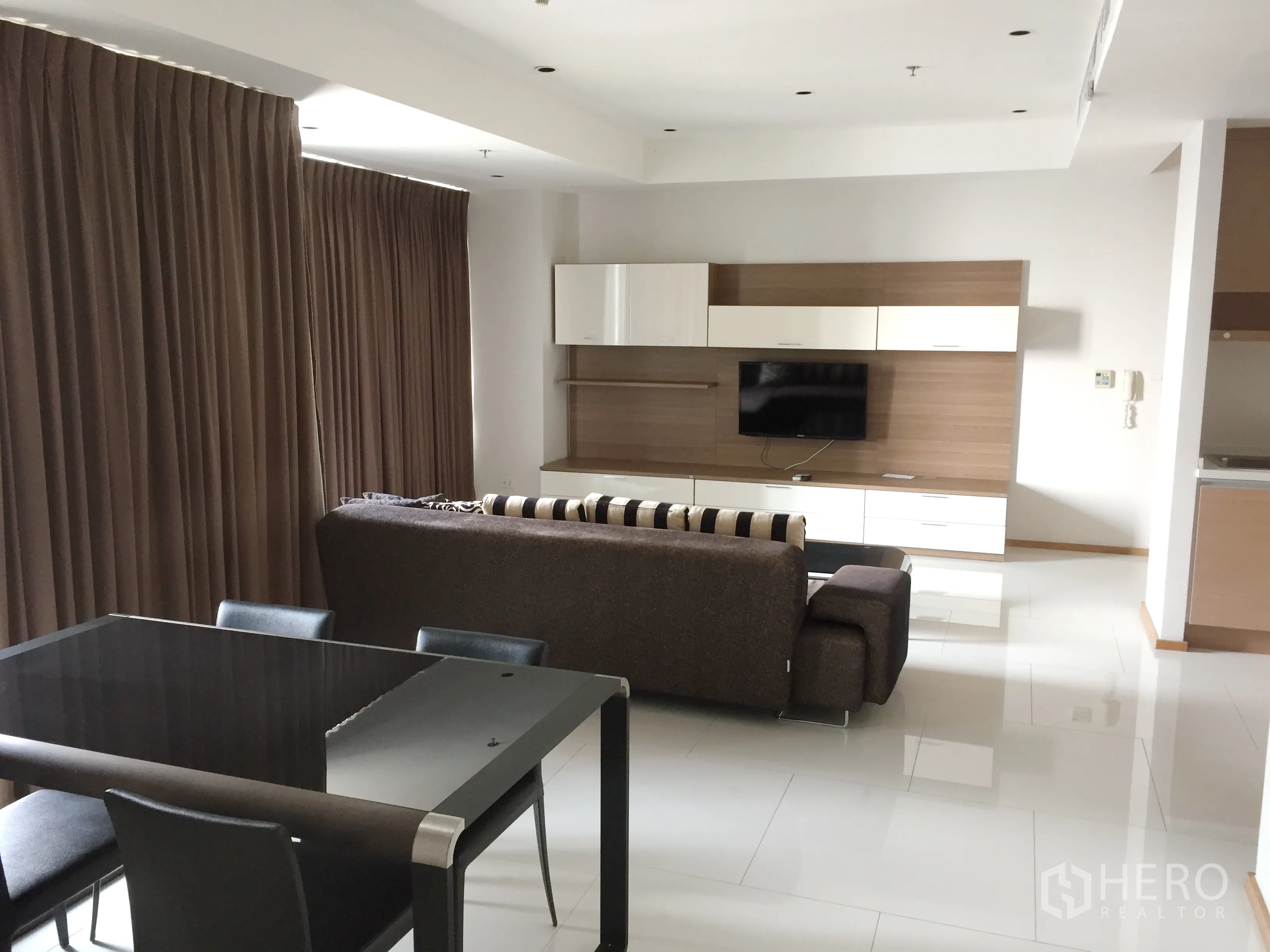 公寓 出租在Khlong Toei, Bangkok - 开放式客厅与餐区，转角沙发、电视墙与落地窗帘的现代公寓。